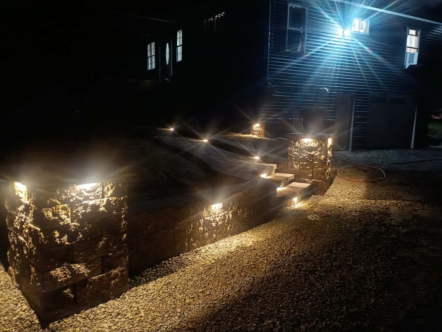 Completed JLStoneworks retaining wall, steps and paver walkway illuminated at night